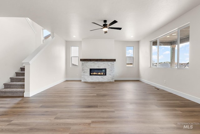 unfurnished living room featuring a ceiling fan, stairs, baseboards, and wood finished floors