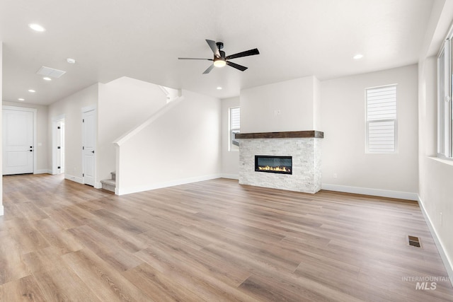 unfurnished living room featuring stairway, a fireplace, visible vents, and light wood finished floors