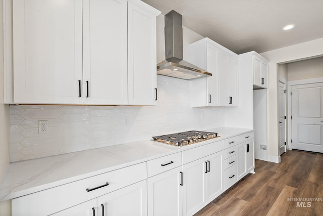 kitchen with dark wood-style flooring, white cabinetry, wall chimney range hood, light stone countertops, and stainless steel gas stovetop