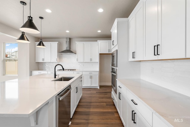 kitchen with dark wood-style floors, appliances with stainless steel finishes, white cabinetry, a sink, and wall chimney exhaust hood