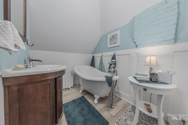 bathroom featuring vanity, wood-type flooring, vaulted ceiling, radiator heating unit, and a tub