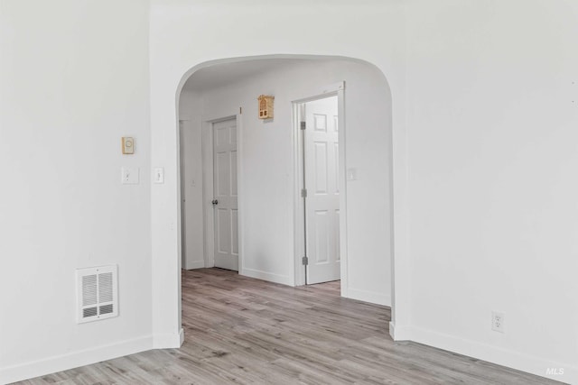 empty room featuring arched walkways, baseboards, and light wood-style flooring