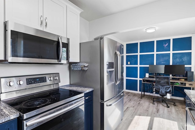 kitchen with appliances with stainless steel finishes, light wood-type flooring, white cabinetry, light stone countertops, and a desk