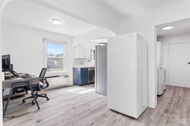 office space featuring light wood-type flooring, washer / dryer, and arched walkways