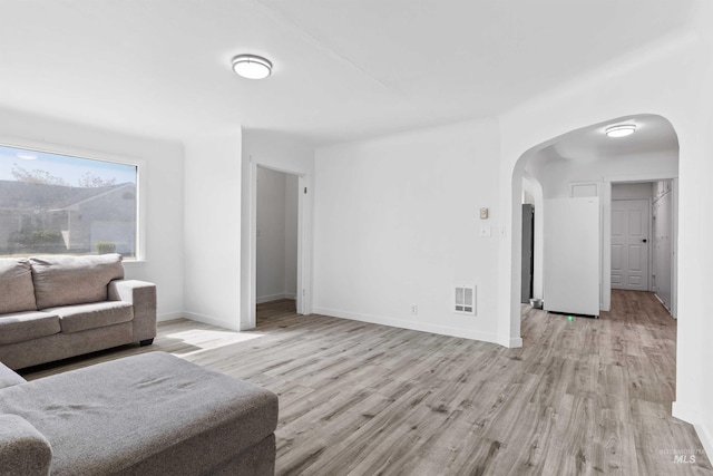 living room featuring arched walkways, light wood-style flooring, and baseboards