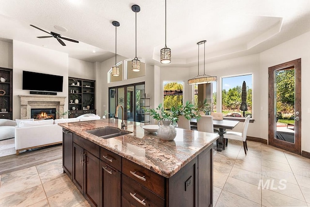 kitchen with a sink, light tile patterned flooring, dark brown cabinetry, and light stone counters