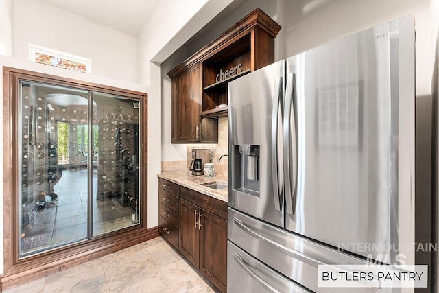 kitchen featuring stainless steel fridge with ice dispenser, open shelves, a sink, dark brown cabinetry, and light stone countertops