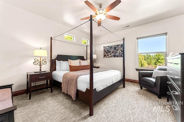 bedroom featuring multiple windows, baseboards, light colored carpet, and ceiling fan