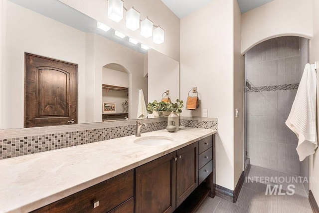 bathroom featuring vanity, decorative backsplash, a tile shower, baseboards, and tile patterned floors