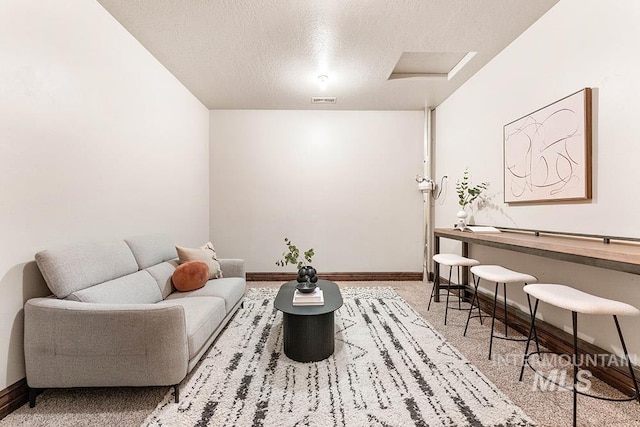 living area with a textured ceiling, attic access, baseboards, and carpet