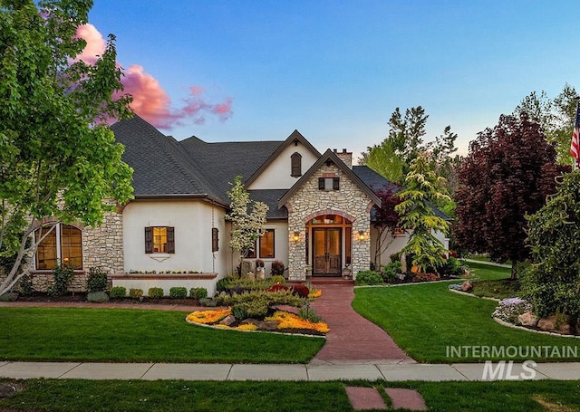 french country home with stone siding, stucco siding, a chimney, a lawn, and french doors
