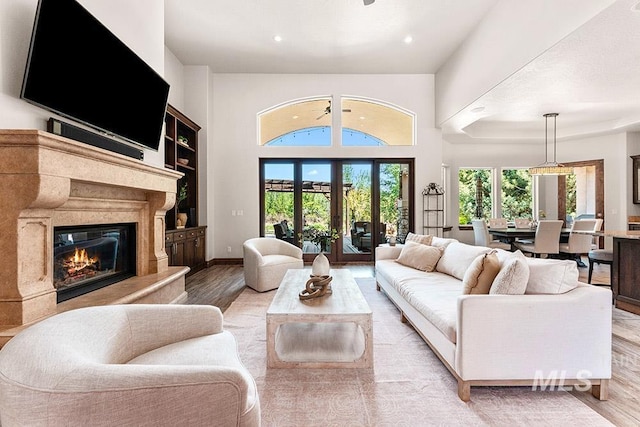 living room featuring light wood-type flooring, a premium fireplace, recessed lighting, a high ceiling, and baseboards