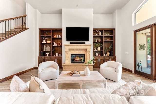 living area with baseboards, wood finished floors, a glass covered fireplace, and stairs