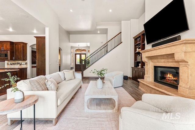 living room featuring arched walkways, light wood-style floors, stairway, a glass covered fireplace, and recessed lighting