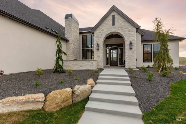 11473 N 17th Way, Boise, ID 83714 - view of exterior entry with stone siding, a chimney, stucco siding, and a shingled roof