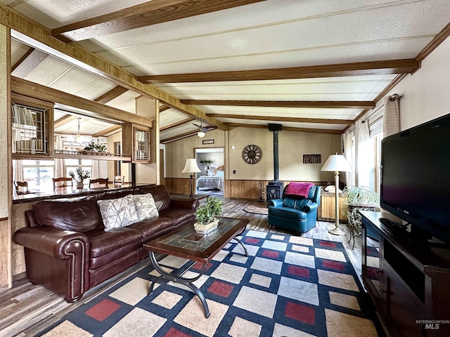 living room with lofted ceiling with beams, ceiling fan, plenty of natural light, and a wood stove