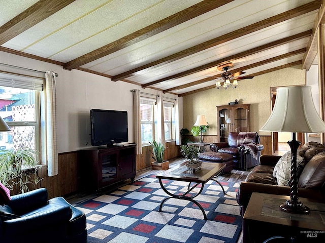 living room with a wealth of natural light, wooden walls, ceiling fan, and vaulted ceiling with beams