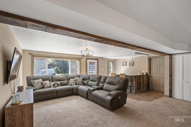 carpeted living room featuring a textured ceiling, beamed ceiling, a chandelier, and bar area