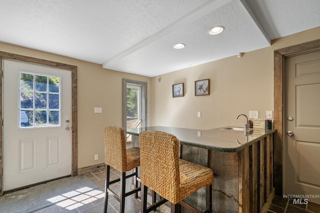 bar area with a textured ceiling, recessed lighting, a sink, baseboards, and stone finish floors