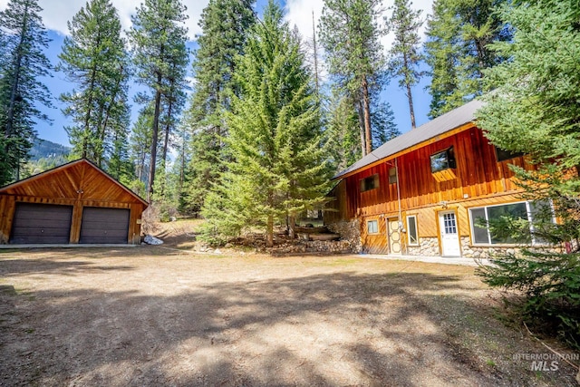 view of front of house with stone siding, a garage, an outdoor structure, and board and batten siding