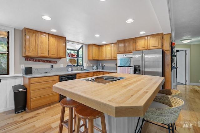 kitchen featuring black electric stovetop, oven, light wood-type flooring, recessed lighting, and a sink