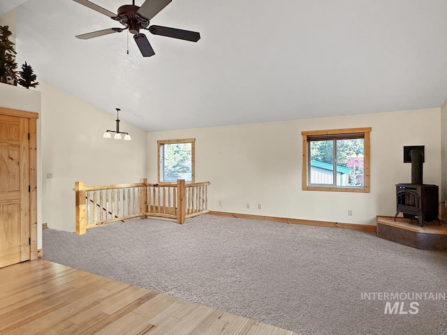 unfurnished living room featuring ceiling fan, a wood stove, baseboards, lofted ceiling, and light wood-type flooring