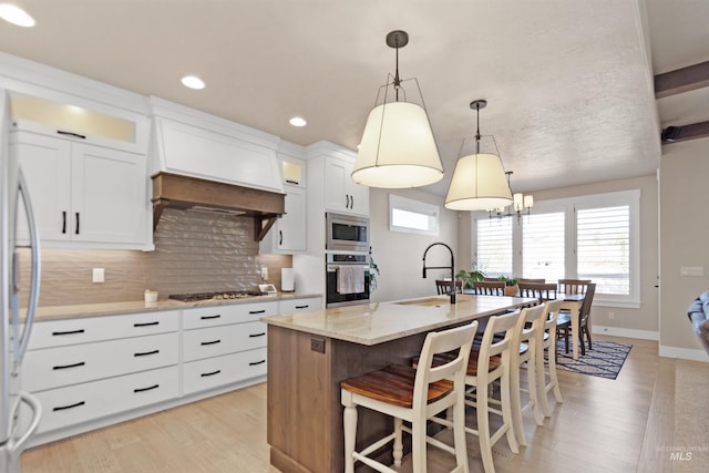 kitchen with a center island with sink, backsplash, appliances with stainless steel finishes, a sink, and premium range hood