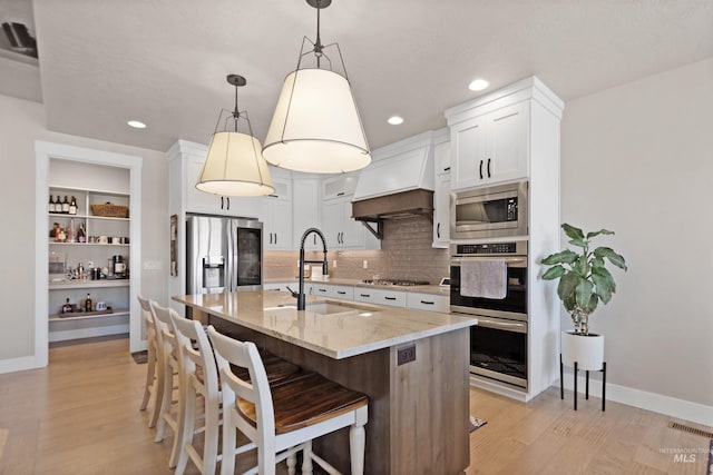 kitchen with visible vents, light stone counters, stainless steel appliances, premium range hood, and a sink