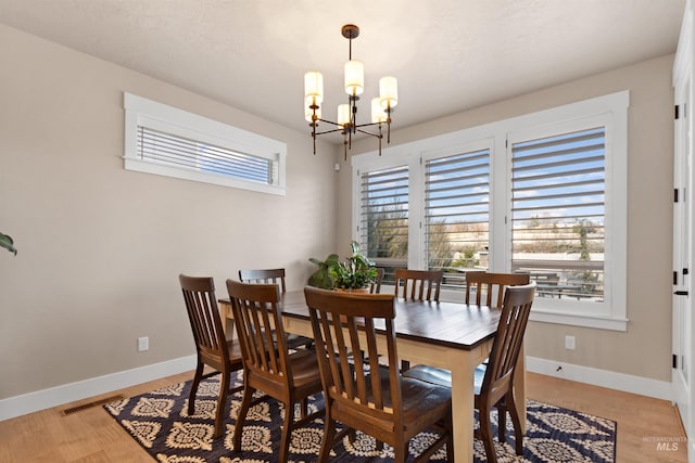 dining room featuring visible vents, light wood finished floors, baseboards, and an inviting chandelier