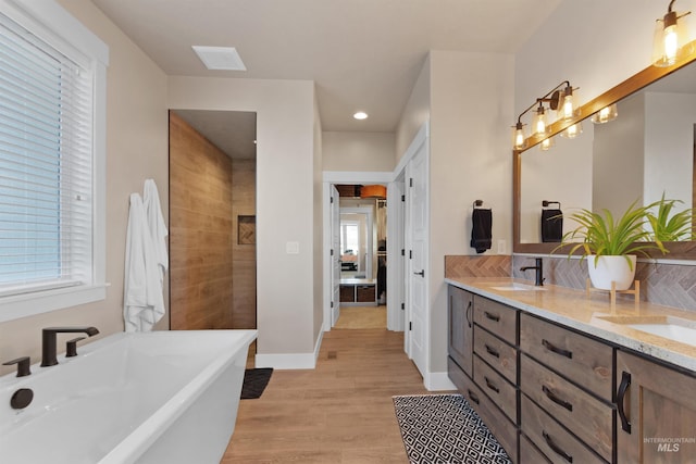 full bath with double vanity, a soaking tub, a sink, wood finished floors, and baseboards