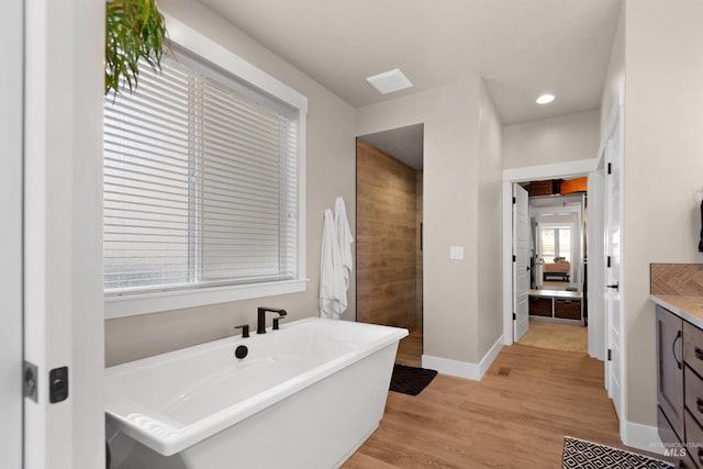 bathroom with baseboards, wood finished floors, a freestanding bath, vanity, and recessed lighting