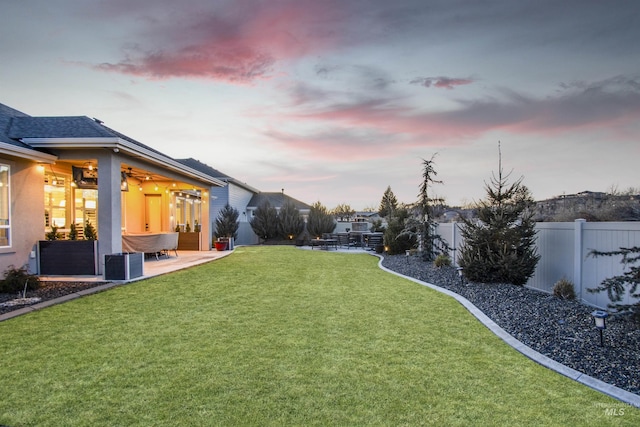 yard at dusk featuring a patio area, a fenced backyard, and central air condition unit