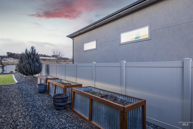 property exterior at dusk featuring fence, a garden, and stucco siding