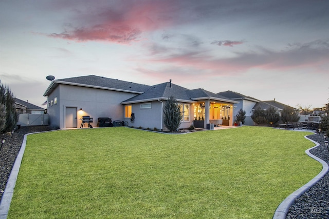 back of house featuring roof with shingles, stucco siding, a lawn, a patio area, and a fenced backyard