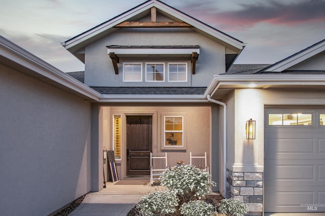 property entrance featuring a shingled roof, stone siding, an attached garage, and stucco siding