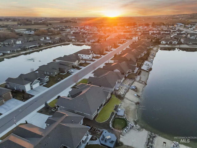 aerial view at dusk featuring a water view and a residential view