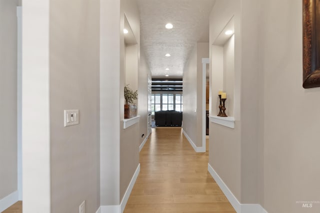 corridor with light wood-type flooring, a textured ceiling, baseboards, and recessed lighting