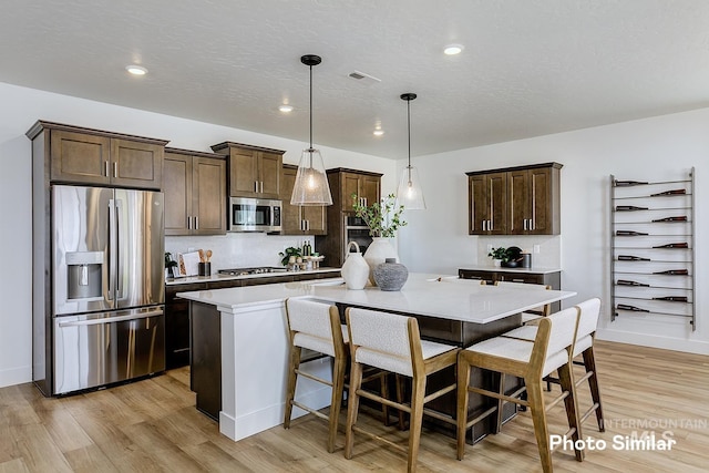 5543 E Bridal Veil Falls Dr, Nampa, ID 83686 - kitchen featuring stainless steel appliances, dark brown cabinets, a kitchen island with sink, light wood-style floors, and a breakfast bar