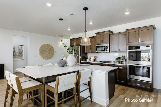 5543 E Bridal Veil Falls Dr, Nampa, ID 83686 - kitchen with appliances with stainless steel finishes, a sink, dark brown cabinetry, light wood finished floors, and a kitchen island with sink