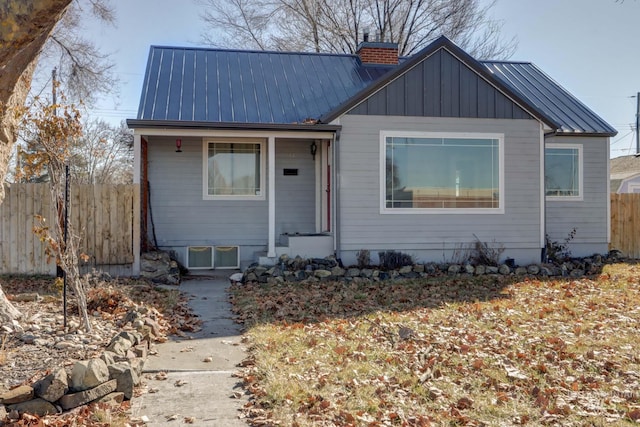 bungalow with a chimney, board and batten siding, a standing seam roof, metal roof, and fence