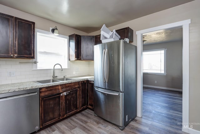 kitchen featuring light wood-style flooring, a sink, dark brown cabinets, appliances with stainless steel finishes, and decorative backsplash