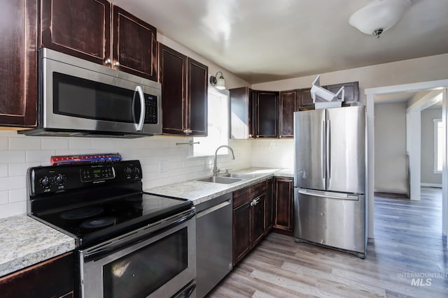 kitchen with light countertops, light wood-style flooring, appliances with stainless steel finishes, a sink, and dark brown cabinets