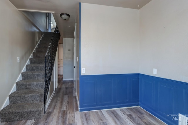 empty room featuring visible vents, stairway, wood finished floors, and wainscoting