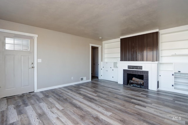 unfurnished living room featuring built in features, visible vents, baseboards, wood finished floors, and a brick fireplace