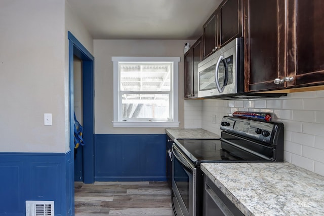 kitchen with dark brown cabinetry, visible vents, a wainscoted wall, stainless steel appliances, and light countertops