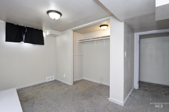 unfurnished bedroom with a textured ceiling, carpet floors, visible vents, baseboards, and a closet