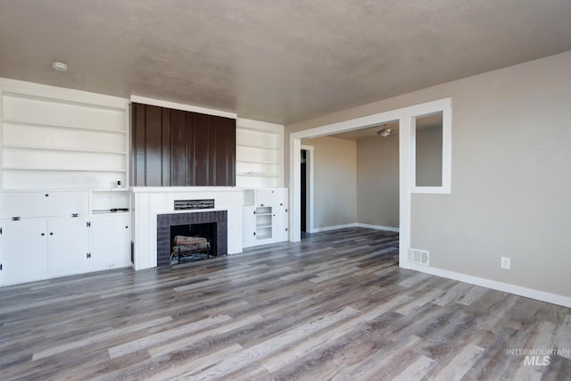 unfurnished living room featuring built in shelves, a fireplace, visible vents, wood finished floors, and baseboards