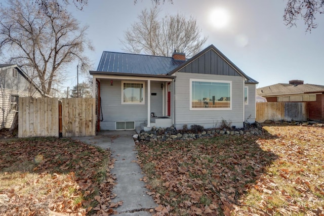 bungalow-style home with metal roof, board and batten siding, a chimney, and fence