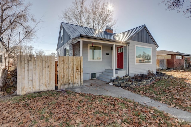 bungalow-style house featuring a standing seam roof, metal roof, board and batten siding, and fence