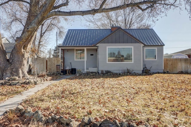 view of front of house featuring board and batten siding, metal roof, a chimney, and fence